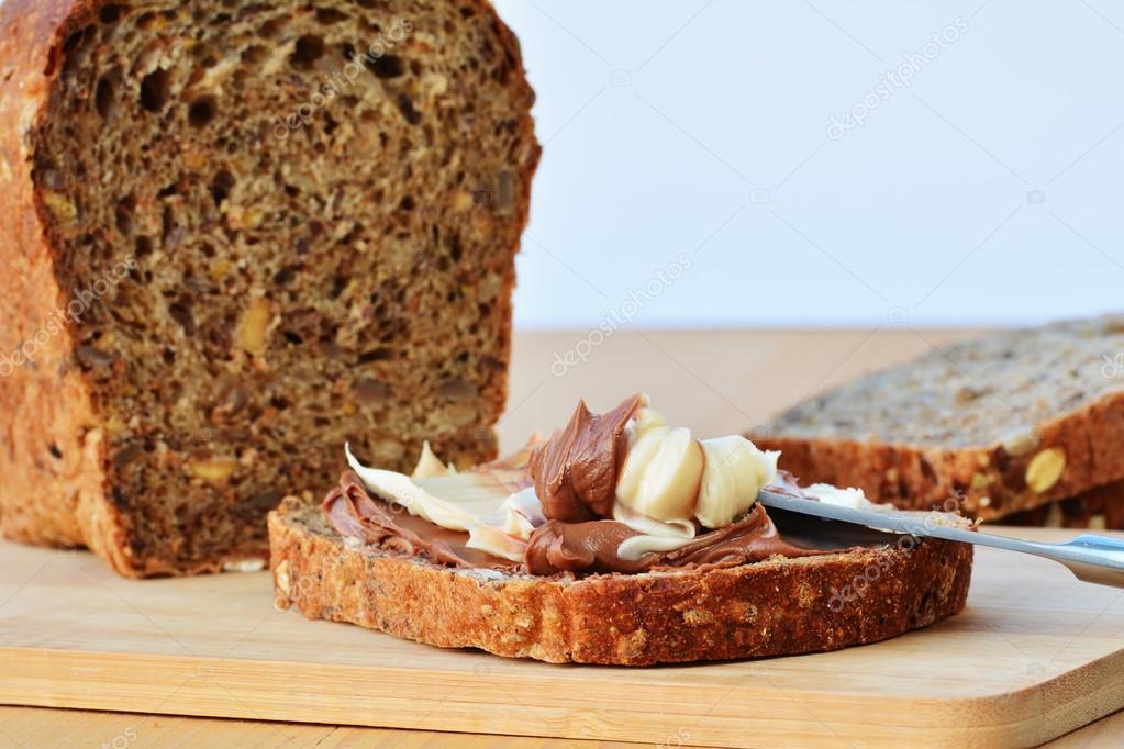 Rebanadas de pan con mantequilla de frutos secos y frutos secos alrededor.